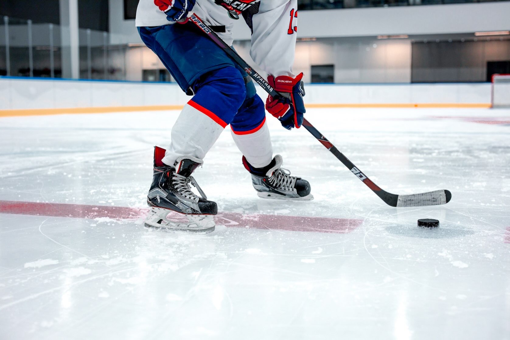 Aspiring hockey player poised to hit a puck with a hockey stick, wearing a blue and red uniform during winter in Dallas.