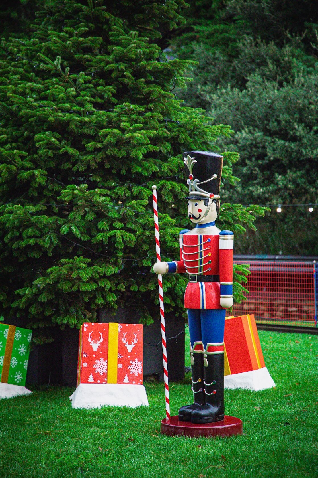Winter in Dallas Christmas display with a life-size wooden soldier beside a large decorated tree and oversized wrapped gifts.
