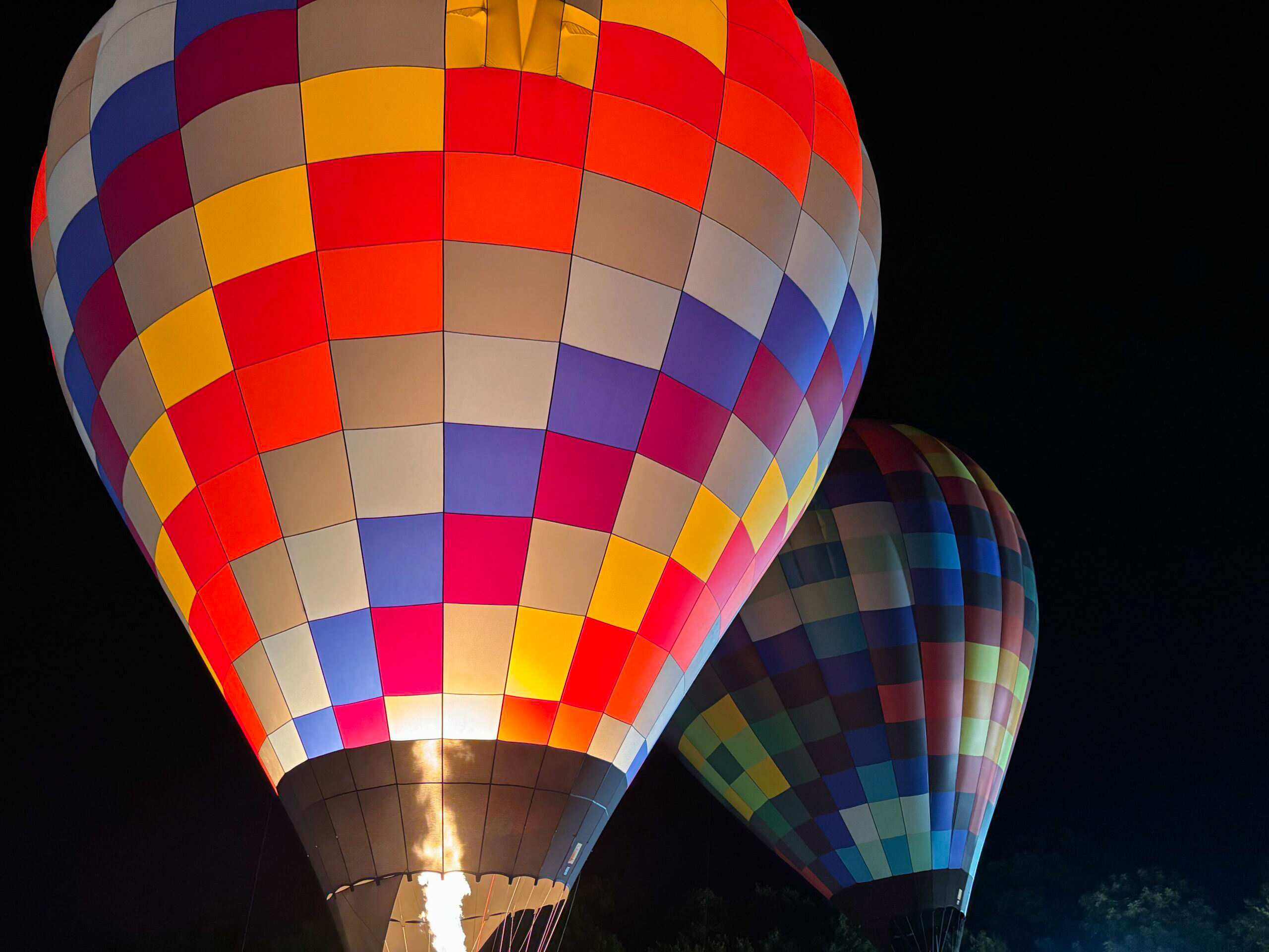 Vibrant red and multicolored hot air balloon rises at the Plano Balloon Festival, with its burner blazing and another colorful balloon in the background, a unique-things-to-do-in-dfw experience.