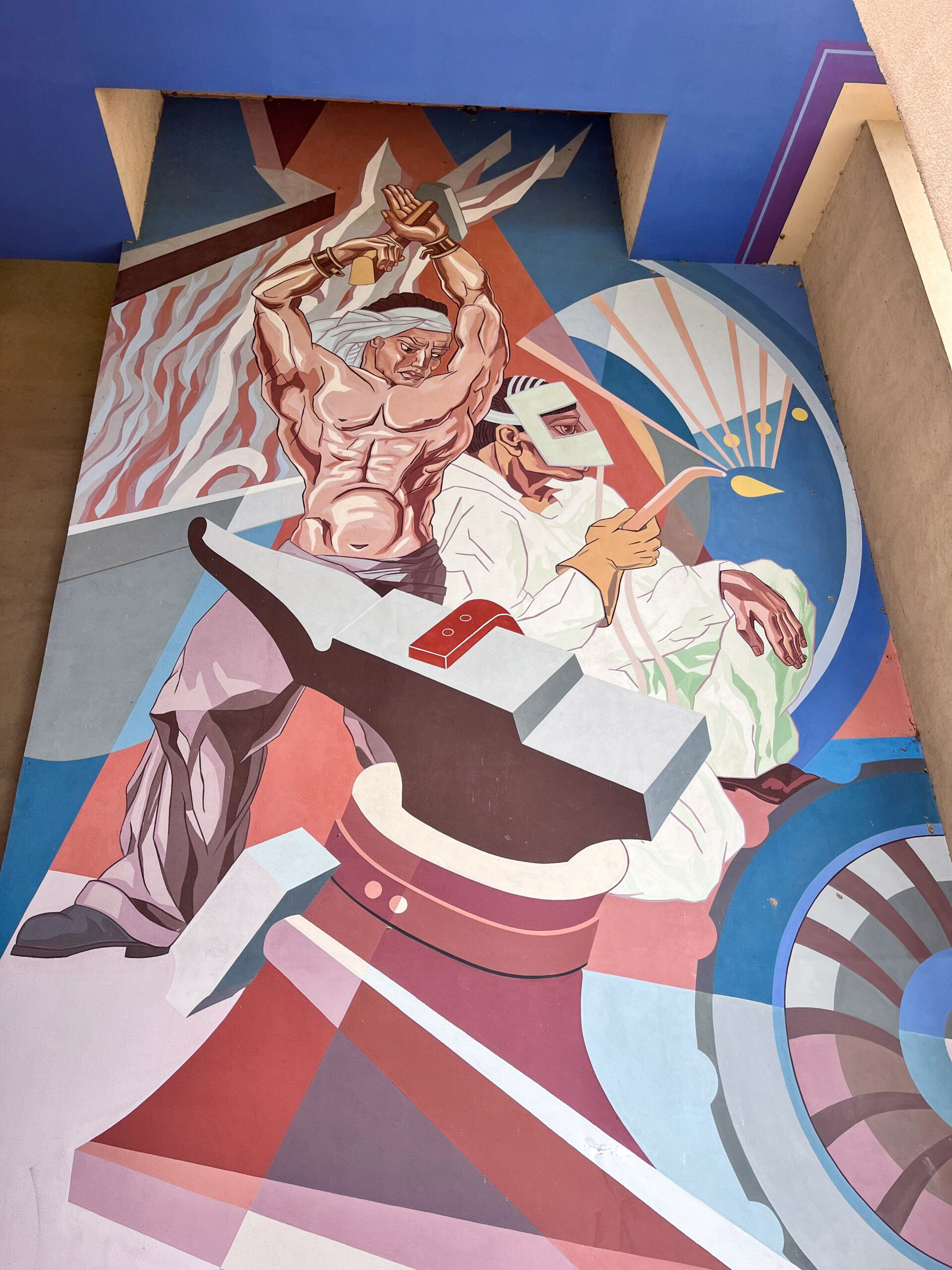 A colorful Fair Park mural depicts a muscular worker raising a tool overhead beside a welder in protective gear, one of many unique-things-to-do-in-dfw.