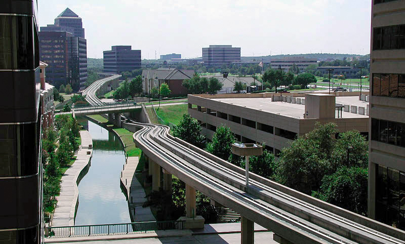 Peaceful view of the Mandalay Canal in Las Colinas, with calm water, lush greenery, and surrounding buildings.