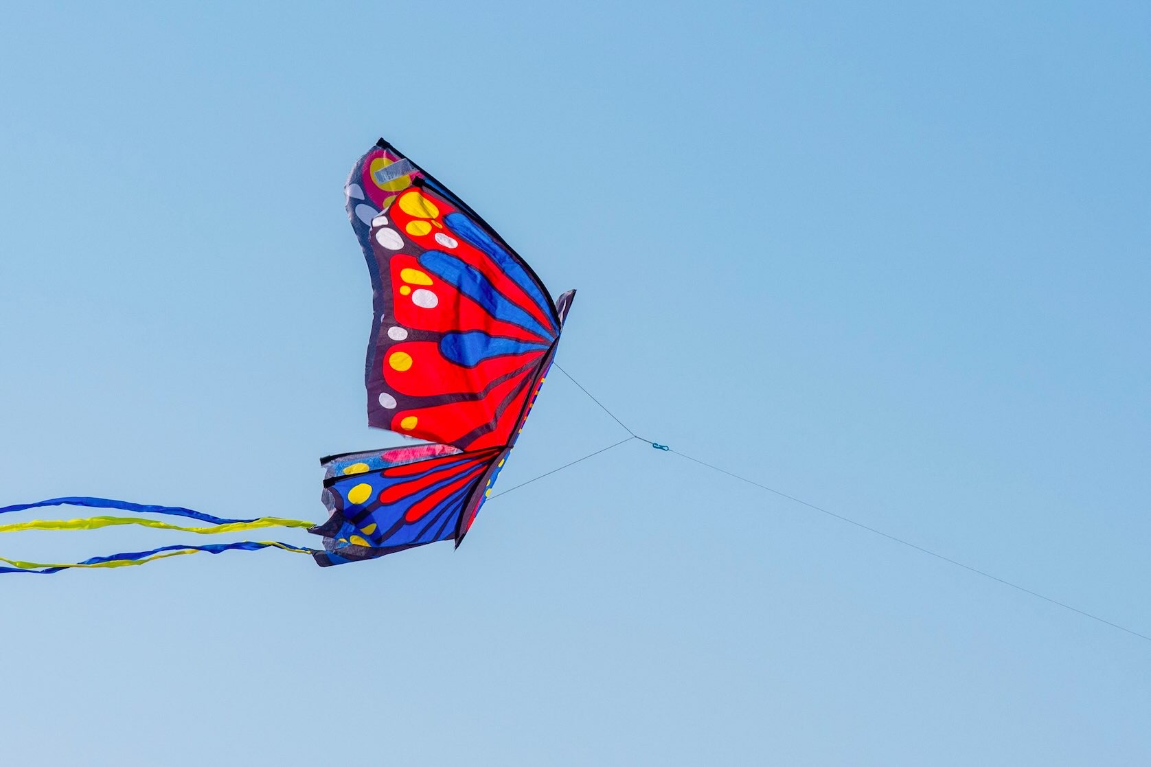 Colorful butterfly kite with red wings and blue and yellow streamers flying against a blue sky at White Rock Lake, a fun outdoor date idea for couples seeking free things to do in Dallas.